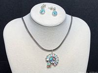 Photo showing three jewelry pieces: pendant on chain and pair of post drop earrings on white display stand.