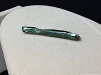 Front side view of the rough, dark green vivianite crystal against a light background showing shiny texture and crystal striations.