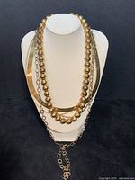 Five necklaces displayed on white bust against black background