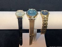 Three wristwatches displayed together: two Movado Museum models and one Burgi Flower diamond dial watch.