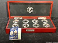 The full set of eight silver plated coins in a wood display box with hinged lid, black foam insert, and coin key booklet.