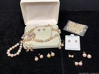 Full set of pearl jewelry displayed in an open box on black fabric including necklace, earrings, and loose pearls in a bag.