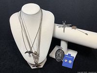 Variety of sterling silver jewelry items displayed including necklaces with bird, fish, shell pendants, dragonfly brooch and others.