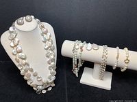 Photo showing entire seven-piece pearl jewelry set: multiple necklaces with large and coin-shaped pearls, faceted glass beads, two pairs of pearl post earrings, and pearl bracelets on display stands.