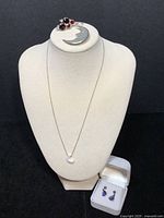 Four jewelry pieces on display: black opal crescent moon pendant on gold plated chain, crescent moon pin with garnet and smoky quartz stones, two pairs of earrings one with smoky quartz and garnet wire, one with trilliant blue-purple stones