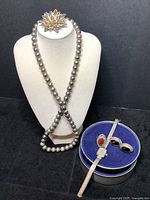 Front view of jewelry displayed on white bust stand showing sterling silver beaded necklace, filigree flower brooch, onyx and marcasite earrings, carnelian ring, sable quartz watch, and pewter trinket box.