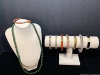 Full lot displayed on necklace bust and bracelet stand: green bead necklace and seven bracelets