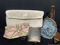 Overview of all four items on black wood surface: silver case, gray/blue purse, pink/cream clutch, white clutch