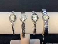 Four vintage Bulova ladies watches displayed on a cream-colored cylindrical display. From left: diamond-accented 10k Gold Filled, 14k Gold yellow tone, 18k Gold yellow tone, 10k Gold Filled bangle-style watch.