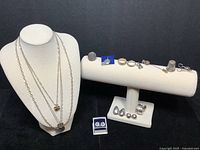 Four necklaces displayed on mannequin with pendants, rings, pins, earrings, sewing scissors pin, and thimble on white jewelry bar.