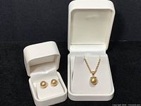 Two white jewelry boxes containing a 10K rope chain with 14K pendant and a pair of yellow pearl post earrings