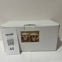 White cardboard box with an image on the side showing the two cat mugs included, sealed and new.