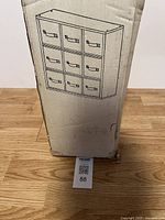 Full view of the boxed 9 drawer hardware organizer with an illustration of the unit on the box showing 3x3 drawer layout.