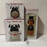 Photo of dog-themed kitchenware boxes showing sponge holder, snack jar, and measuring cups in packaging.