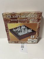 Photo of the original packaging/box showing the glass chess set with wooden case, with an image of the set arranged on the chessboard.