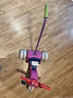 Top view of red and purple kids plastic tricycle with white wheels and rear push handle.