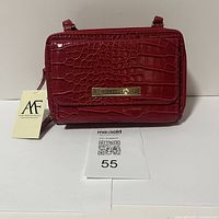 Front view of red crocodile embossed leather purse with metal brand plate and tag visible.