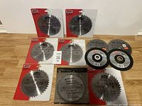 Overview photo showing 11 saw blades and 2 cutting discs, some in packaging others loose on wooden floor.