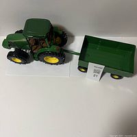 Green John Deere 6420 toy tractor with yellow wheels and attached green trailer, front side view.