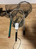 Three vintage fish nets displayed on wooden floor showing frames and handles with black netting.