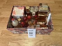 Top down image showing a collection of vintage perfume bottles in a floral box, including a boxed Oscar de la Renta perfume and several used and new bottles of various colors and sizes.
