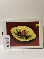 Box showing image of the vintage oval serving plate with cardinal bird design and pine cones on a yellow background.