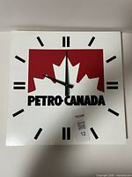 Front view of vintage Petro Canada wall clock, white background, red maple leaf and black text, minimalist hour markers and black hands.