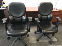 Front view of two black leather executive office chairs side by side showing padded seats, curved backs and armrests.