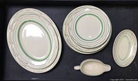 Top view of all plates and gravy boat on a black tray showing oval and round plates arranged in stacks according to size and type.