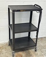 Front view of black Bretford adjustable utility cart with three shelves and wheels, showing cord on top shelf