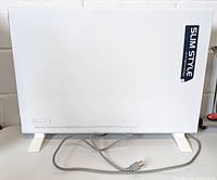 Front side of the DeLonghi Slim Style convection panel heater showing the white smooth panel, feet, and attached power cord.