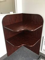 Wooden corner bookshelf with two shelves, dark cherry finish, shown from front angle.