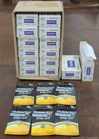 Photo showing multiple cartons of Duracell 370/371 button batteries arranged in a box, with some blister packs displayed in front.