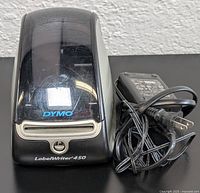 Front view of Dymo LabelWriter 450 label printer with power adapter placed beside it on a flat surface.