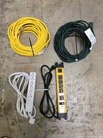 Four items shown: yellow and green outdoor extension cords, white GE 6-outlet extension cord, and Mastercraft yellow and black 6-outlet power bar with cord.