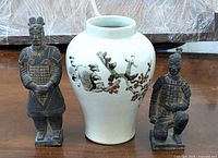 Front view of two Chinese pottery tomb court attendant figurines flanking a vintage Asian ceramic vase with painted bird and blossom design.
