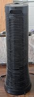 Front view showing tall black cylindrical tower air purifier with ventilation grill all around the body.