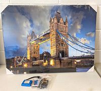 Front view of the framed LED lighted picture showing London Bridge scene, includes LED pack, remote, and power cables displayed in front, with metal corner protectors on the frame.