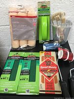 Full lot view showing hand sander, sanding sheets, paint rollers, paint brushes, paint refill pails, and roller handles