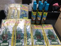 Photo showing multiple Royal Pine tree-shaped Little Trees air fresheners in packaging and several Caribbean Colada scent spray bottles with blue caps.