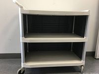 Front view of Rubbermaid 3-shelf utility cart, showing hollow shelves and caster wheels.