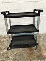 Front and side angled photo of Rubbermaid 3-tier rolling cart showing black plastic shelves and metal supports with caster wheels.