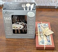 Full view of both boxed items: Reflections 160-piece cutlery set in original packaging and Viva 2-pack decorative spoons in red box with clear window.