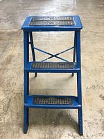 Front view of vintage blue metal Ekco step stool showing three steps with black rubber traction strips, worn and distressed paint.