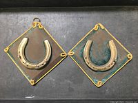 Two vintage cast iron horseshoe wall plaques side by side on gray surface