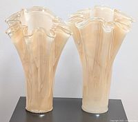 Front view of both vintage apricot gold marble ruffled Murano style glass vases side by side on a dark table showing their elegant color and shape.