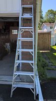 Full view of 8-foot aluminum ladder standing upright outside a garage, showing the entire ladder with all steps and support braces.