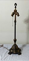 Front view of antique brass lamp showing detailed base, slender body, and dual bulb sockets with pull chains.