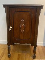 Front view of the antique wooden bedside cabinet showing carved central door panel and turned legs.