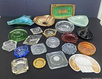 Overview of 17 assorted vintage ashtrays of various colors, shapes, and materials laid out on a black surface